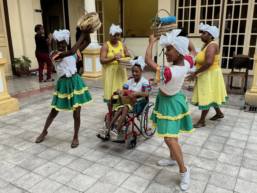 Mehrere Personen mit Körben tanzen um ein Kind im Rollstuhl