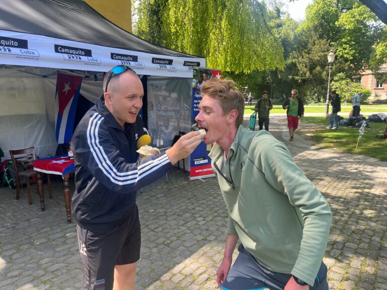 Zwei Männer bei einem Charity-Run, einer füttert den anderen mit einem Löffel Essen.