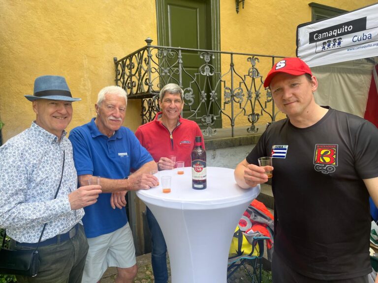 Vier Männer stehen an einem Stehtisch im Freien. Sie halten Getränkebecher in der Hand.