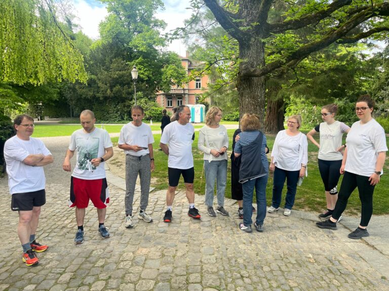 Gruppe von Menschen in Freizeitkleidung steht auf einem gepflasterten Weg in einem Park.